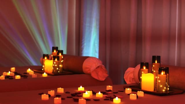 Two massage tables dressed for a couples appointment at Wonder Spa, with candle clusters, rose petals and coloured light on the curtains.