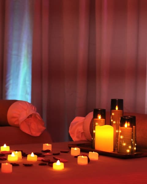 Two massage tables dressed for a couples appointment at Wonder Spa, with candle clusters, rose petals and coloured light on the curtains.