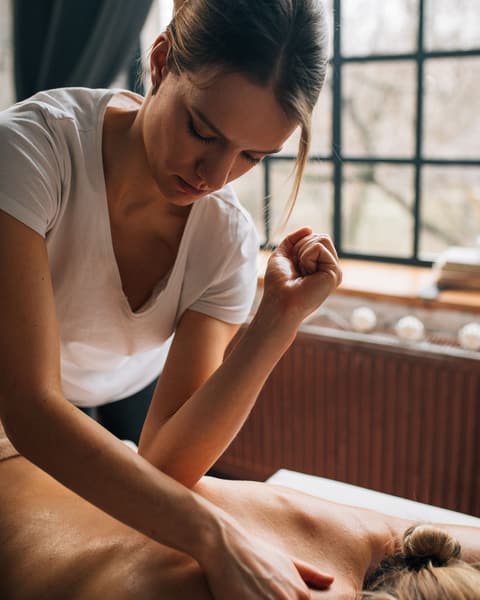 A massage therapist leaning in with firm forearm pressure on a client's back.
