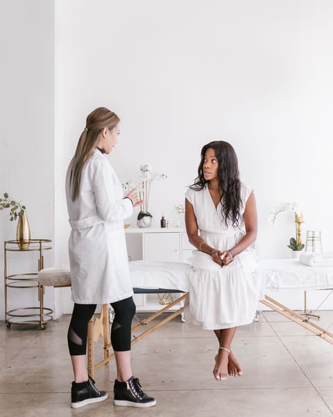 A massage therapist in a white coat talking with a client who sits on a massage table, before a session.