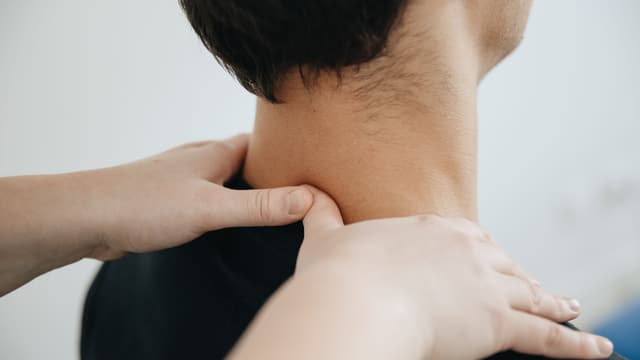 Hands applying focused pressure to the neck and upper shoulder.
